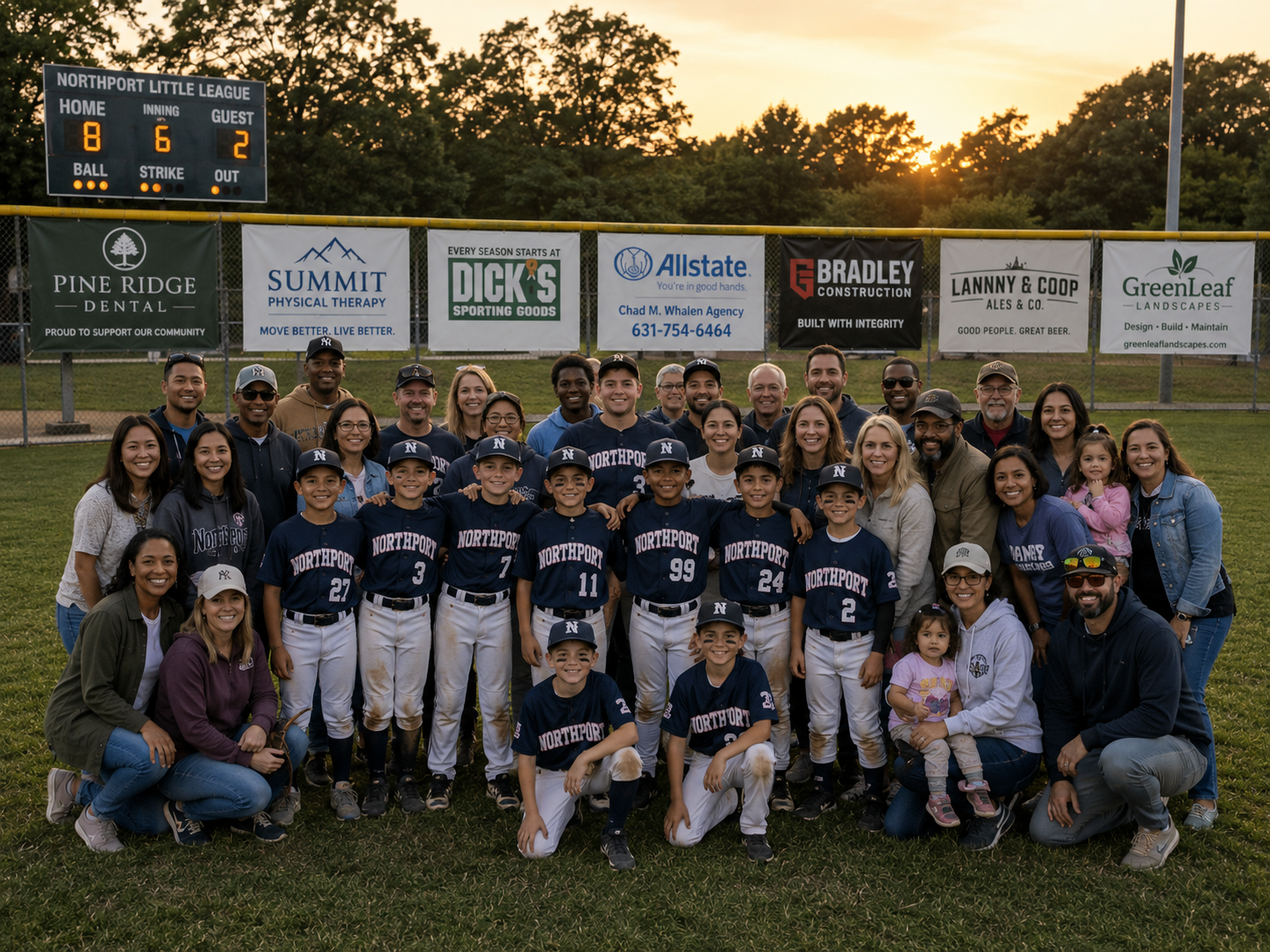 Youth baseball team and their families posing together on the field with sponsor banners behind them